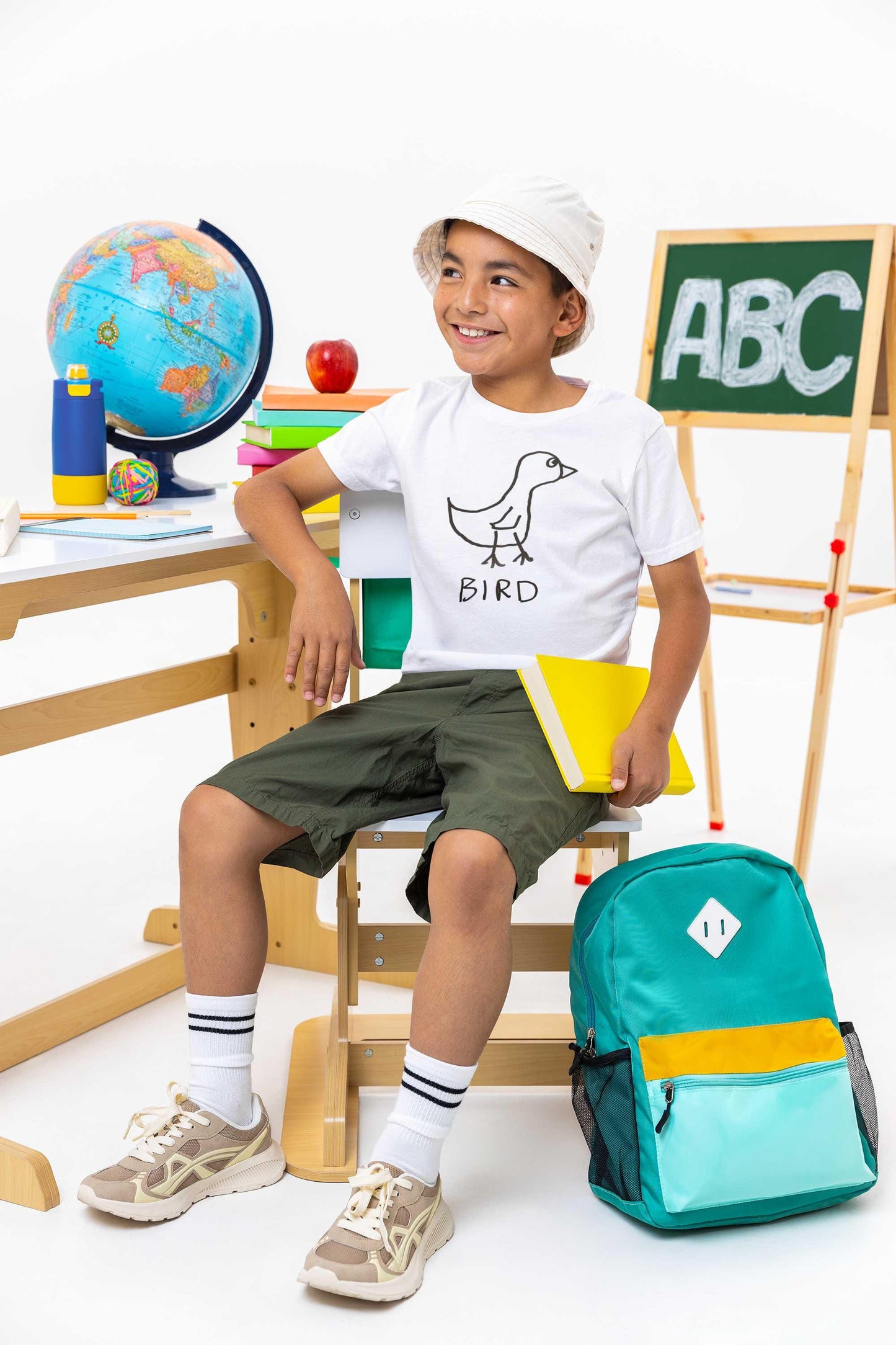 Young boy at his school desk wearing t shirt featuring a crudely drawn black marker drawing of a bird with the word "Bird" underneath