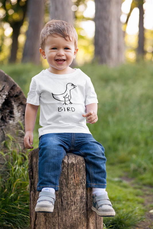 Toddler sitting on a log in a forest wearing a white t-shirt with a hand drawn bird graphic and text.