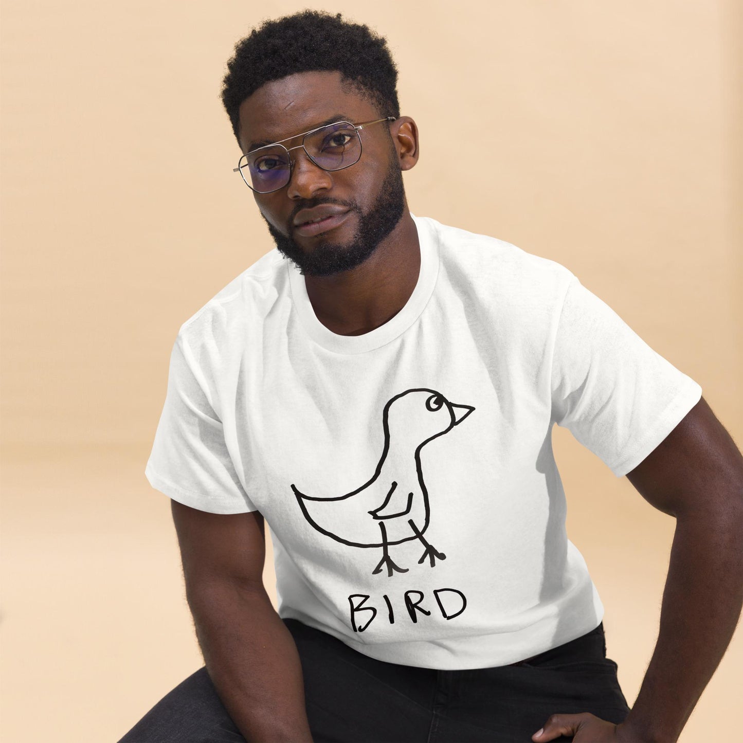 Man wearing a white t-shirt featuring a crude marker drawing of a bird with the word "Bird" underneath on a beige background