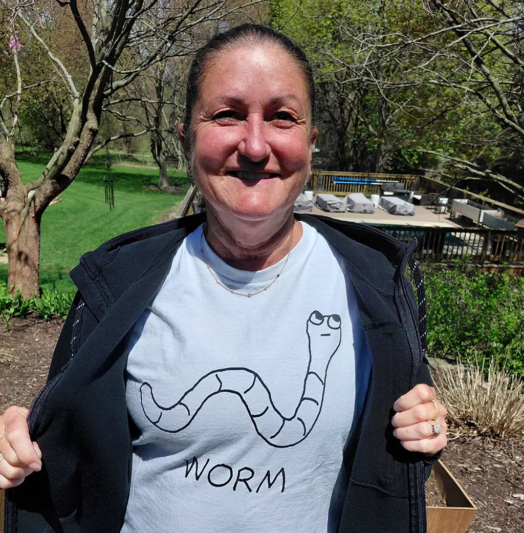 Women in a park on a sunny day, showing off her white t-shirt featuring a lo-fi hand-drawn worm graphic and text.
