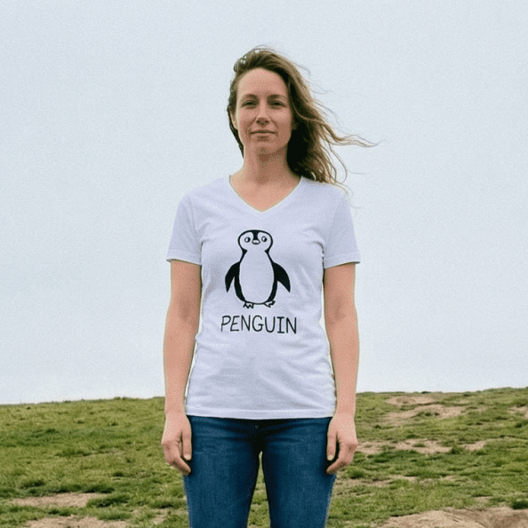Woman standing on a windy grassy field wearing a lo-fi Penguin V-Neck T-Shirt in white