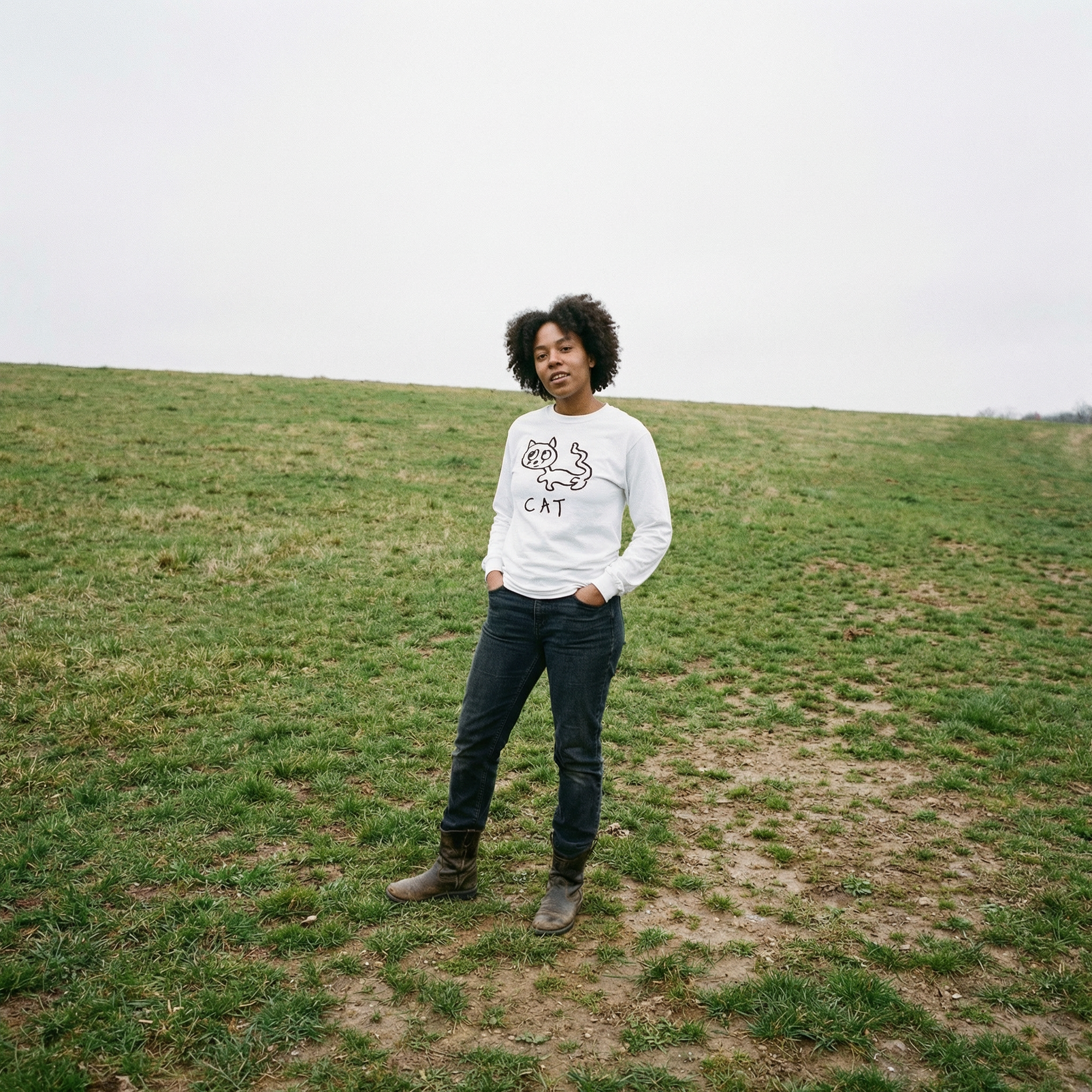 Model in a cat long sleeve tee standing quietly in a soft grassy field