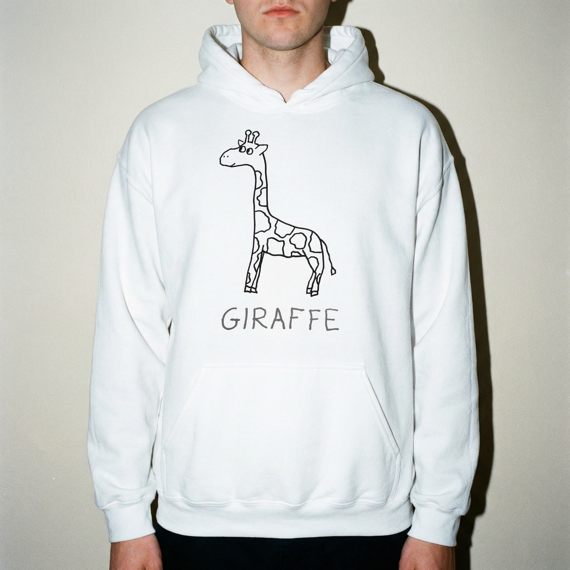 Young man in studio setting wearing a white hoodie with a quirky minimalist lofi giraffe drawing. 