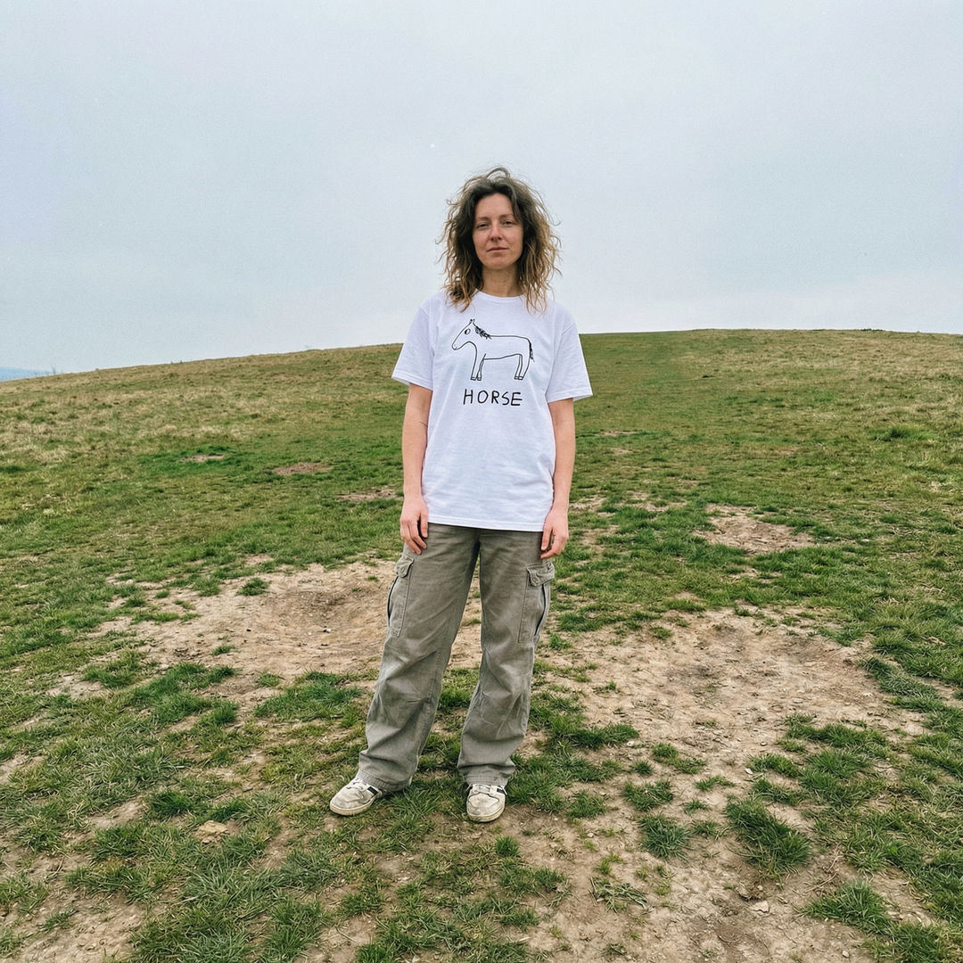Horse shirt worn outdoors  by woman in dark green pants – minimalist lofi horse tee in natural setting