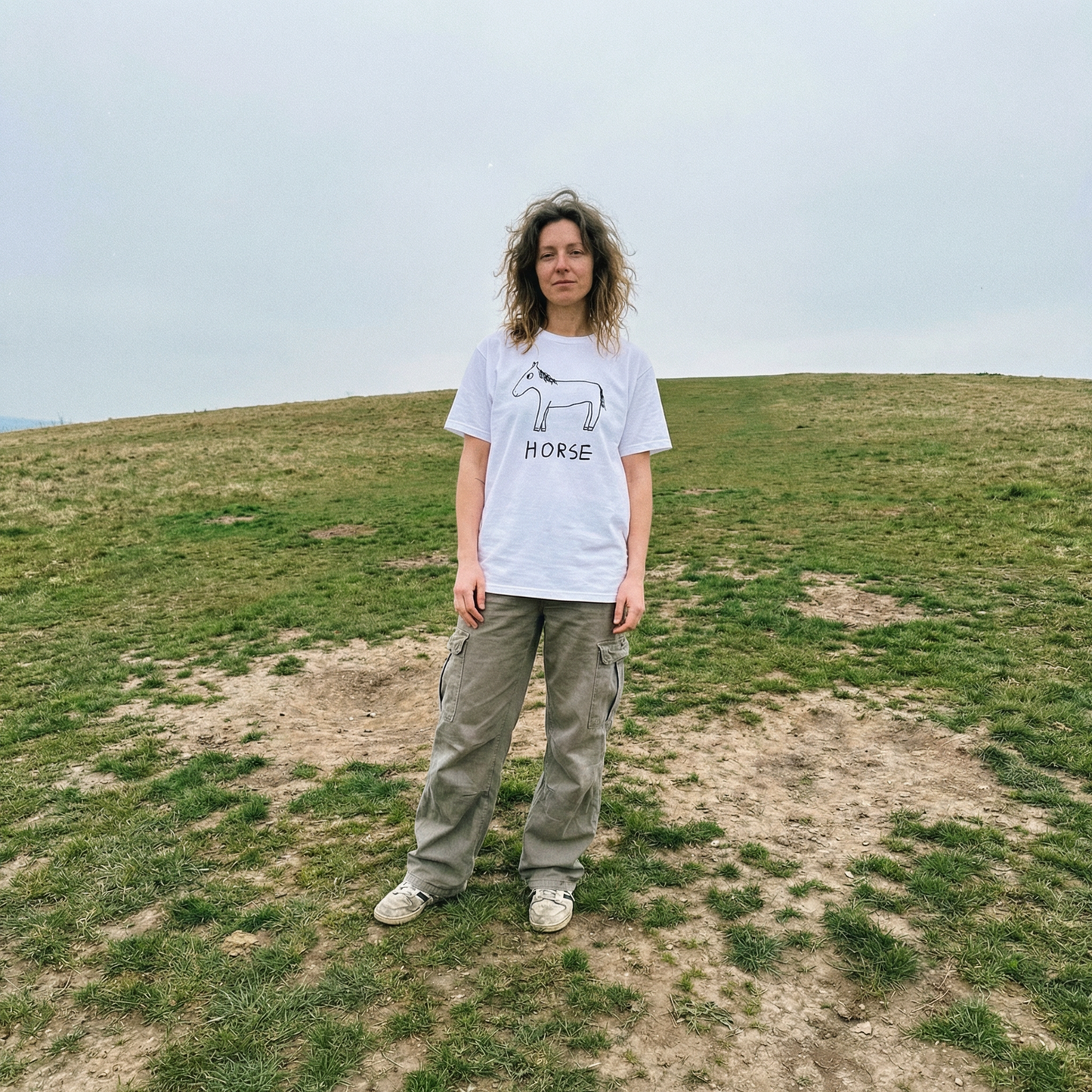 Horse shirt worn outdoors  by woman in dark green pants – minimalist lofi horse tee in natural setting
