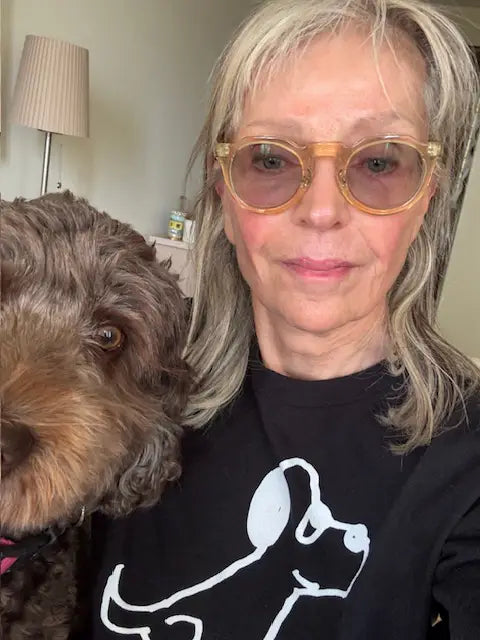 A woman with her brown furry dog. She's wearing a black t-shirt with a lo-fi hand-drawn dog graphic and text. 