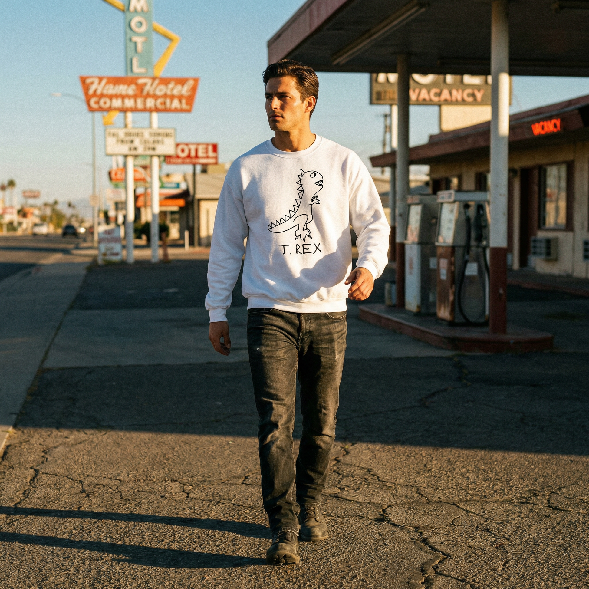 Man wearing a white crewneck sweatshirt with hand drawn T Rex Dinosaur graphic, walking on a street with vintage motel signs in the background
