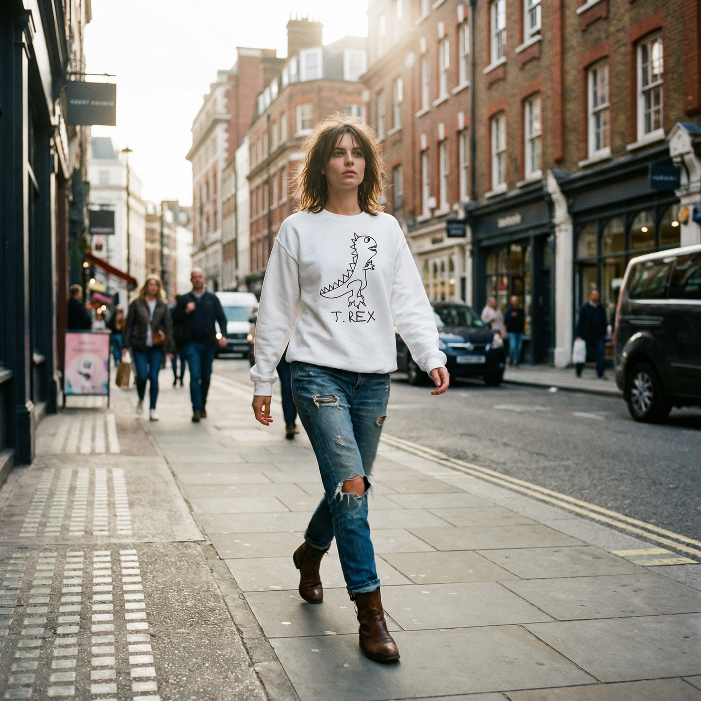 Woman walking on a London Soho street wearing a white crewneck sweatshirt with a hand drawn T Rex Dinasaus graphic design and ripped jeans.