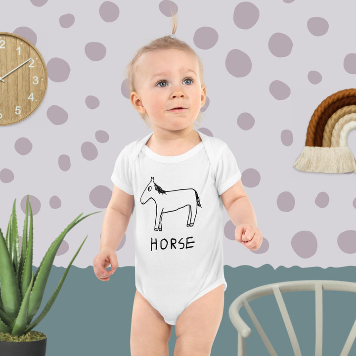 Cute baby in playroom background wearing white bodysuit with a horse drawing.
