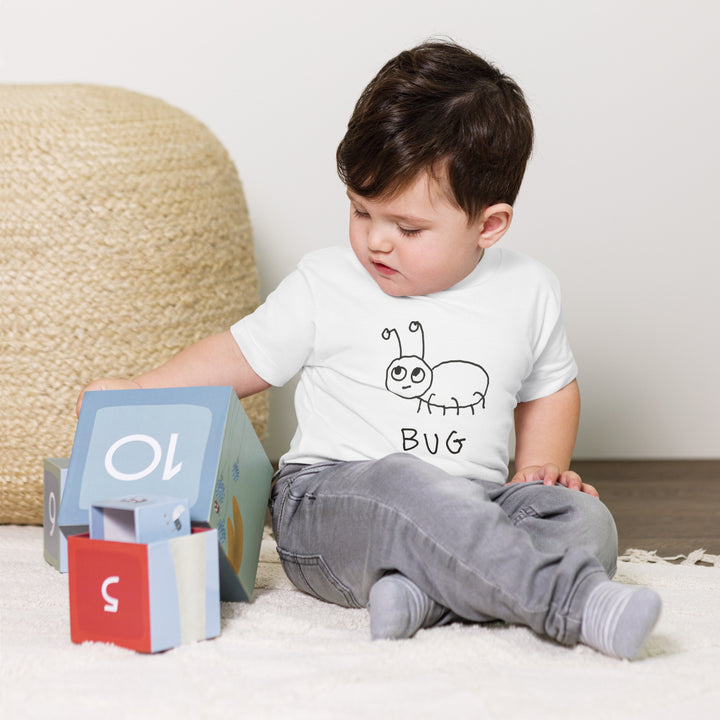 Baby wearing a white t-shirt with a simple hand drawn bug graphic and text "BUG", playing with blocks