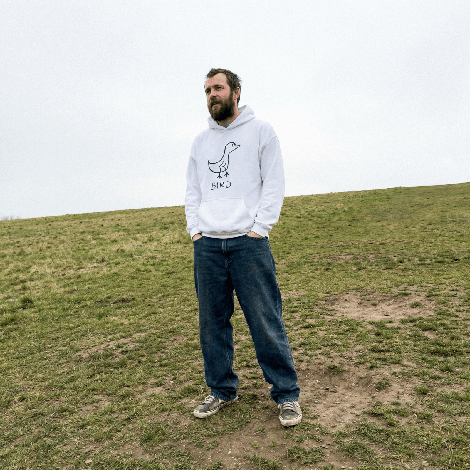 Man standing on a grassy hill wearing a lo-fi Bird Hoodie