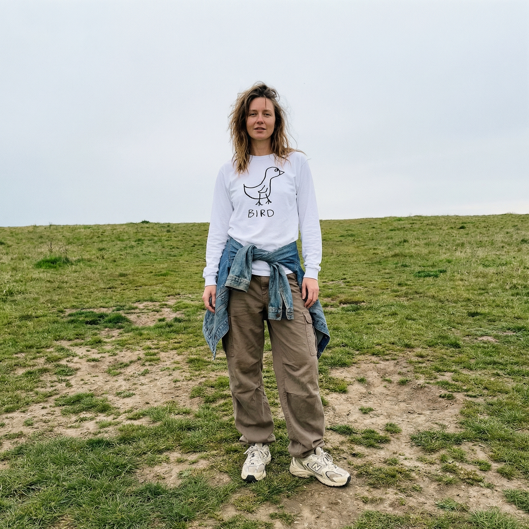 Model wearing a bird long sleeve tee in a grassy field with a wide open sky