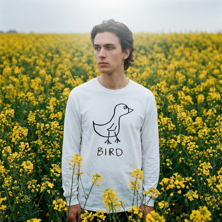 Model in a bird long sleeve tee with arms out in a breezy field of yellow flowers