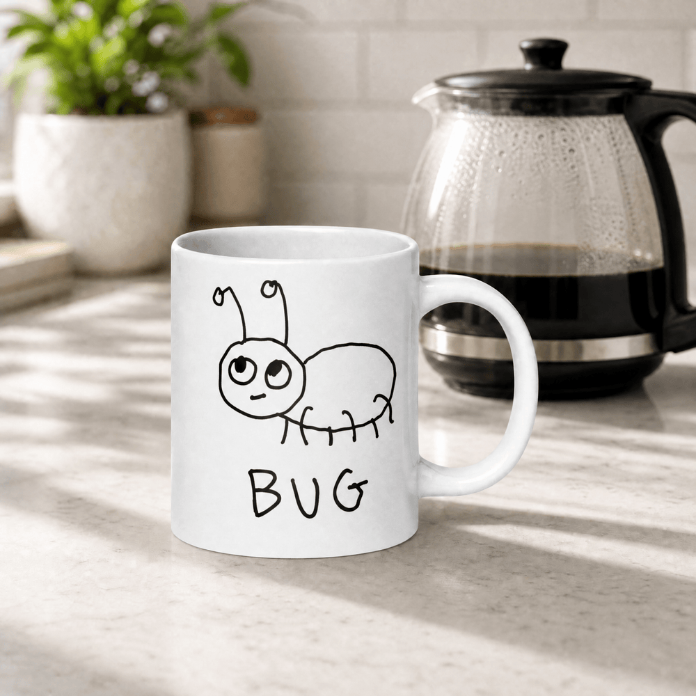 White mug with a lo-fi hand drawn graphic of a bug and text 'BUG' text on a kitchen counter with a coffee maker and plants.