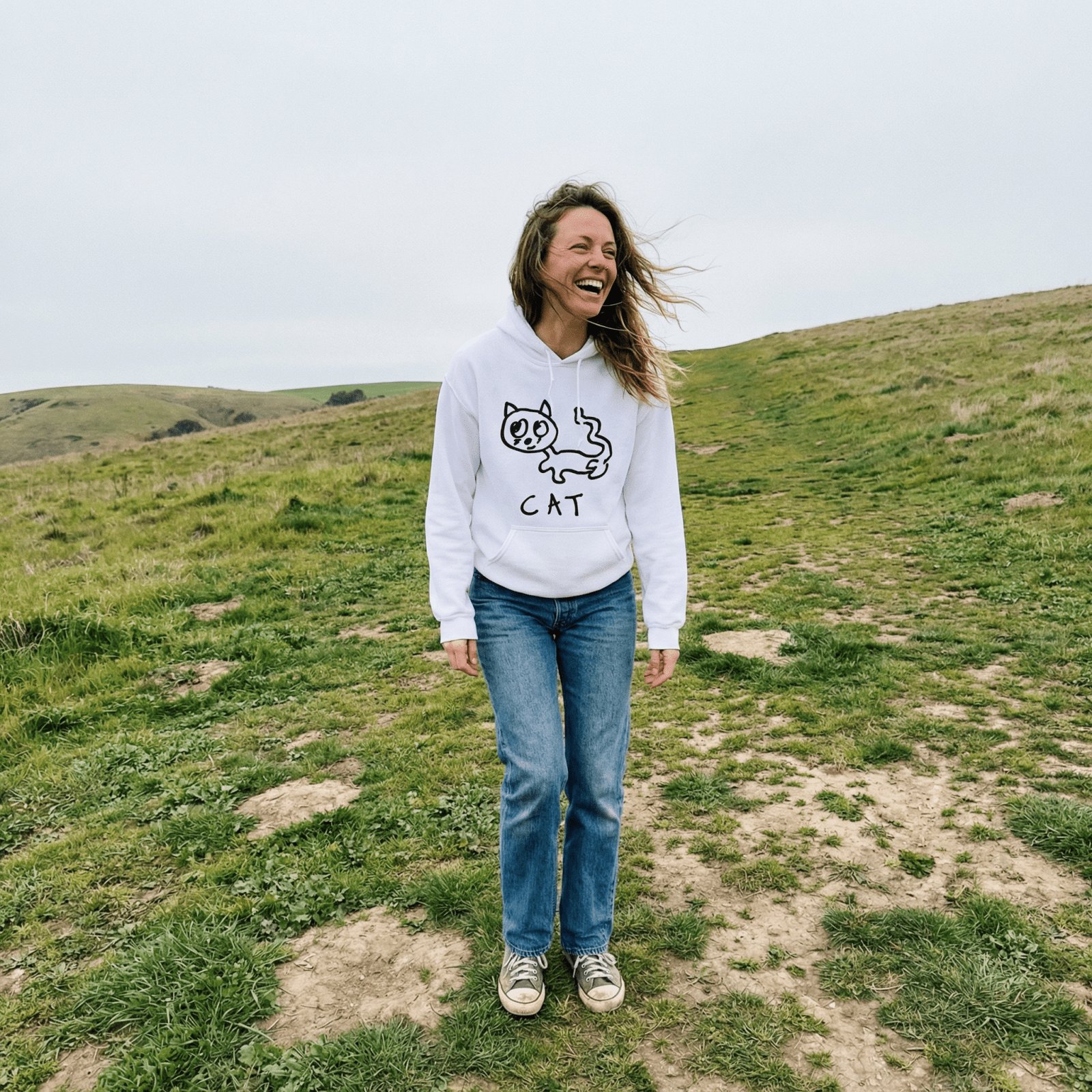 Woman standing on a windswept grassy hill wearing a lo-fi Cat Hoodie
