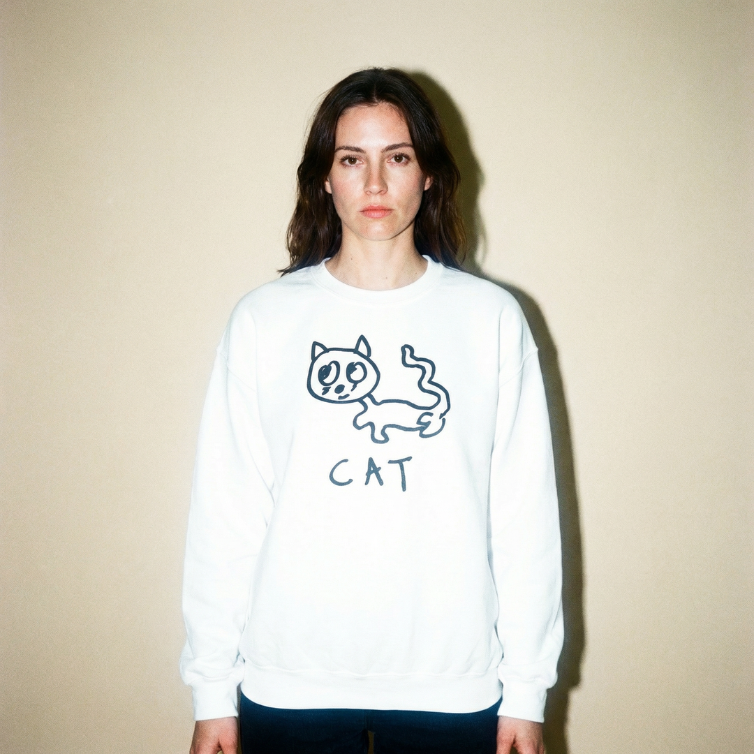 Model in a cat sweatshirt against a light grey backdrop, arms crossed, unbothered look