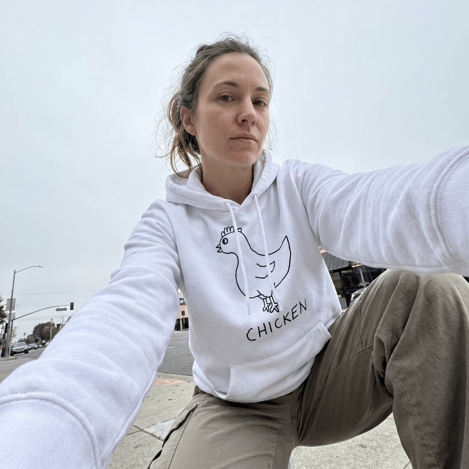 Woman taking a selfie on a city street wearing a lo-fi Chicken Hoodie