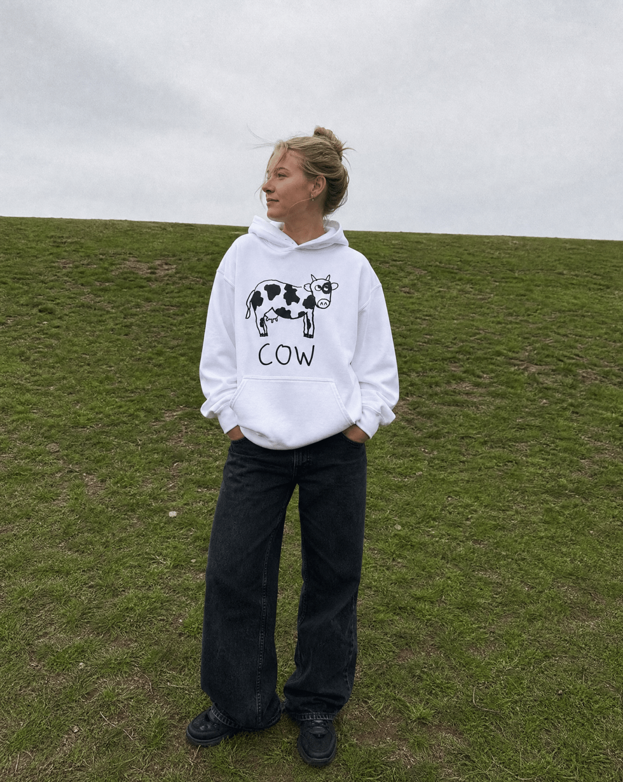 Woman standing on a grassy hill wearing a lo-fi Cow Hoodie
