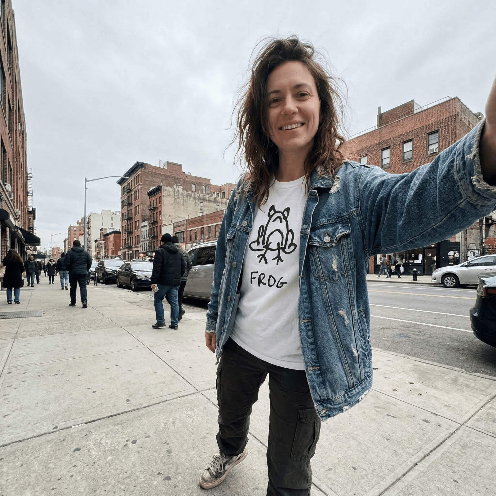 Woman in a denim jacket taking a selfie on a city street wearing a lo-fi Frog Classic Tee