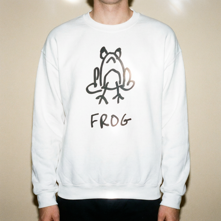 Model wearing a frog sweatshirt against a sage green studio backdrop, relaxed fit