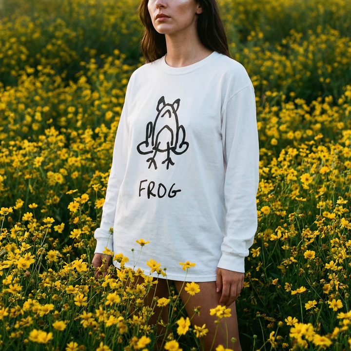 Model wearing a frog long sleeve tee standing in a bright field of yellow flowers