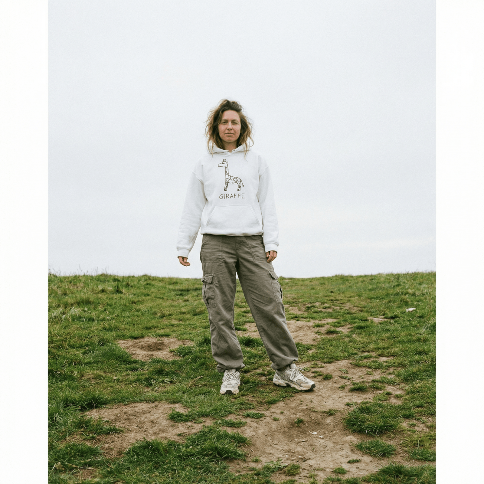 Person standing on a grassy hill wearing a lo-fi Giraffe Hoodie in white