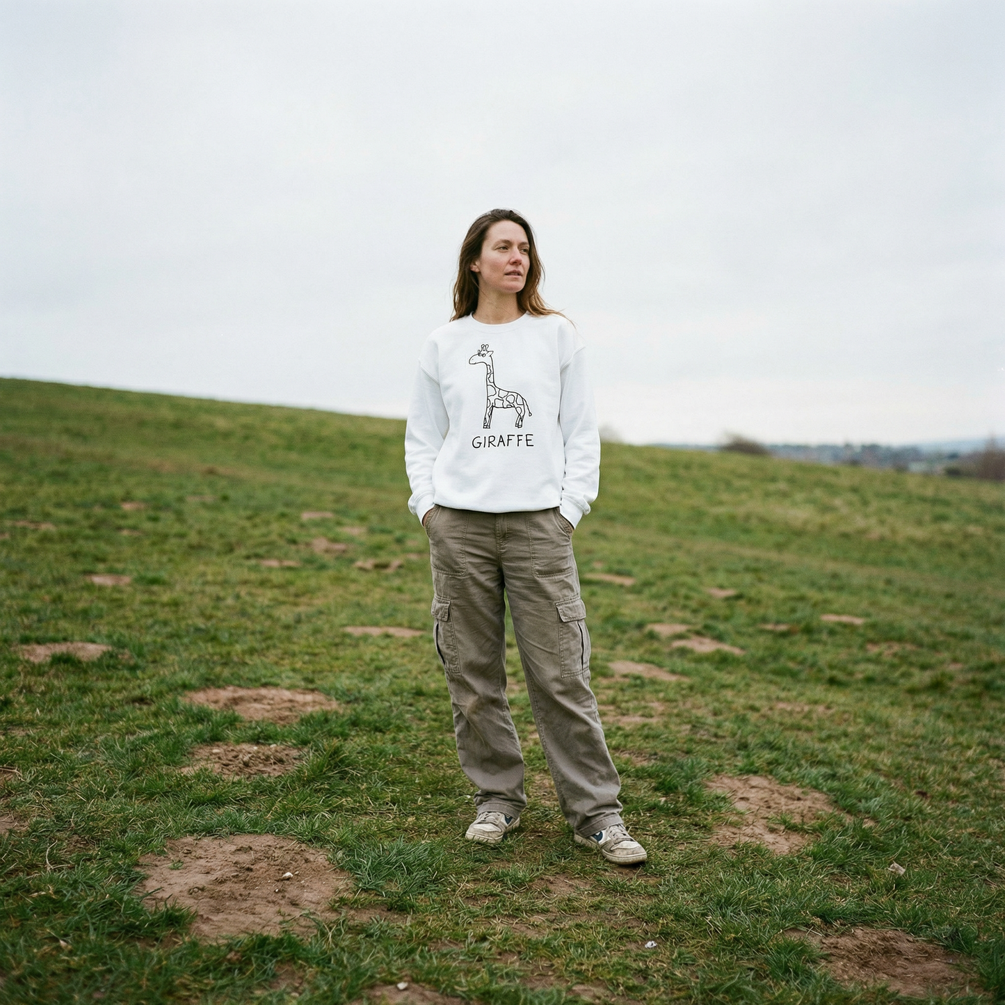 Model in a white crewneck giraffe sweatshirt in an open field, tall grass, wide sky, easy stance