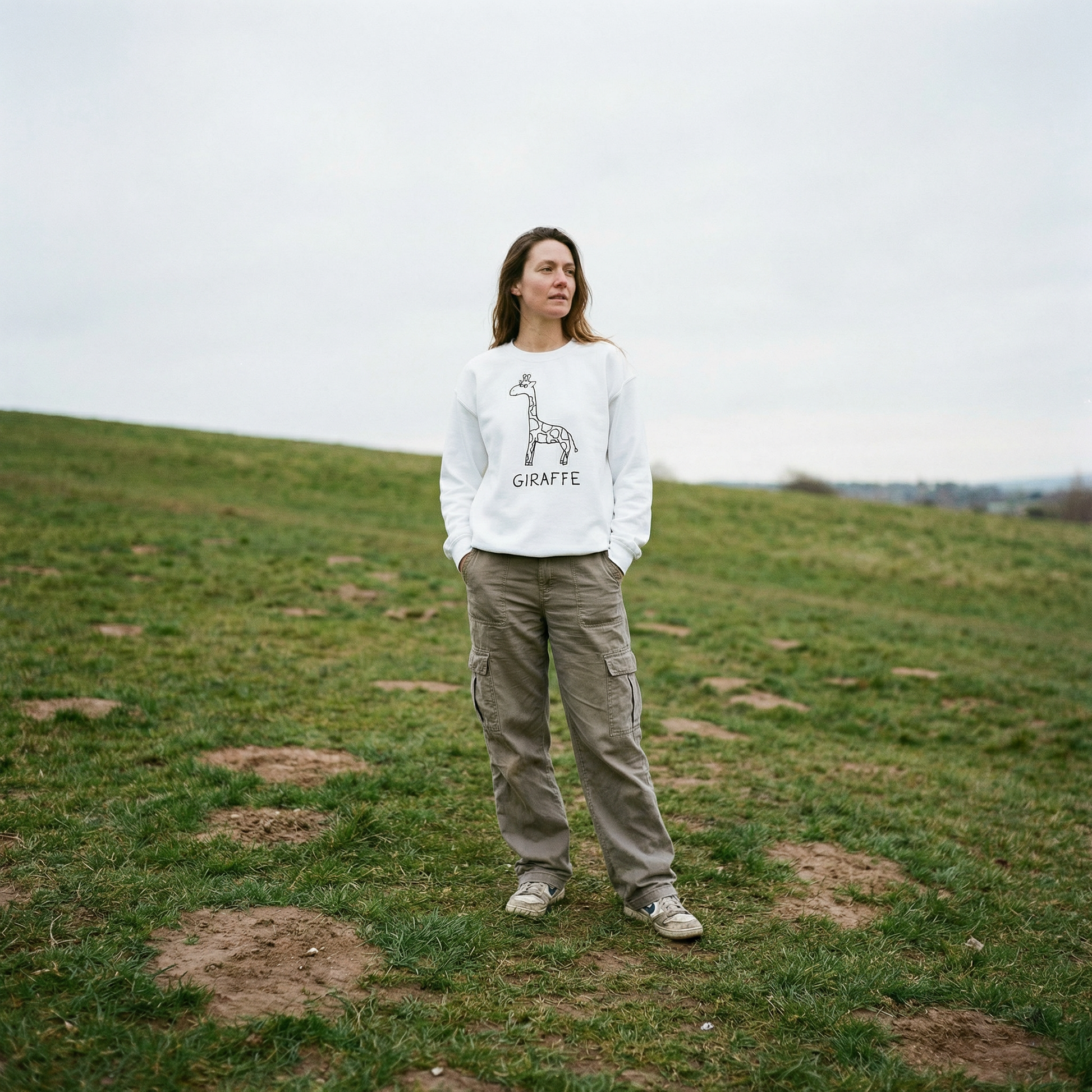 Model in a white crewneck giraffe sweatshirt in an open field, tall grass, wide sky, easy stance