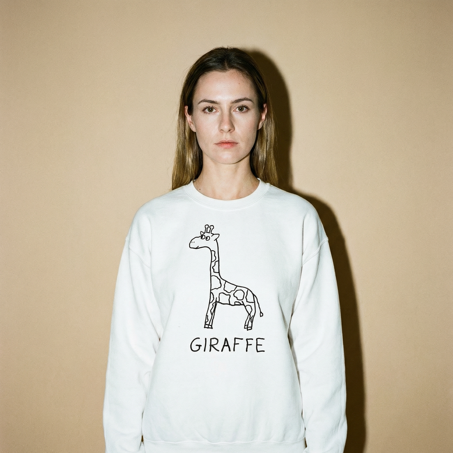 Model in a giraffe sweatshirt against a soft tan backdrop, long neck of a pose, relaxed
