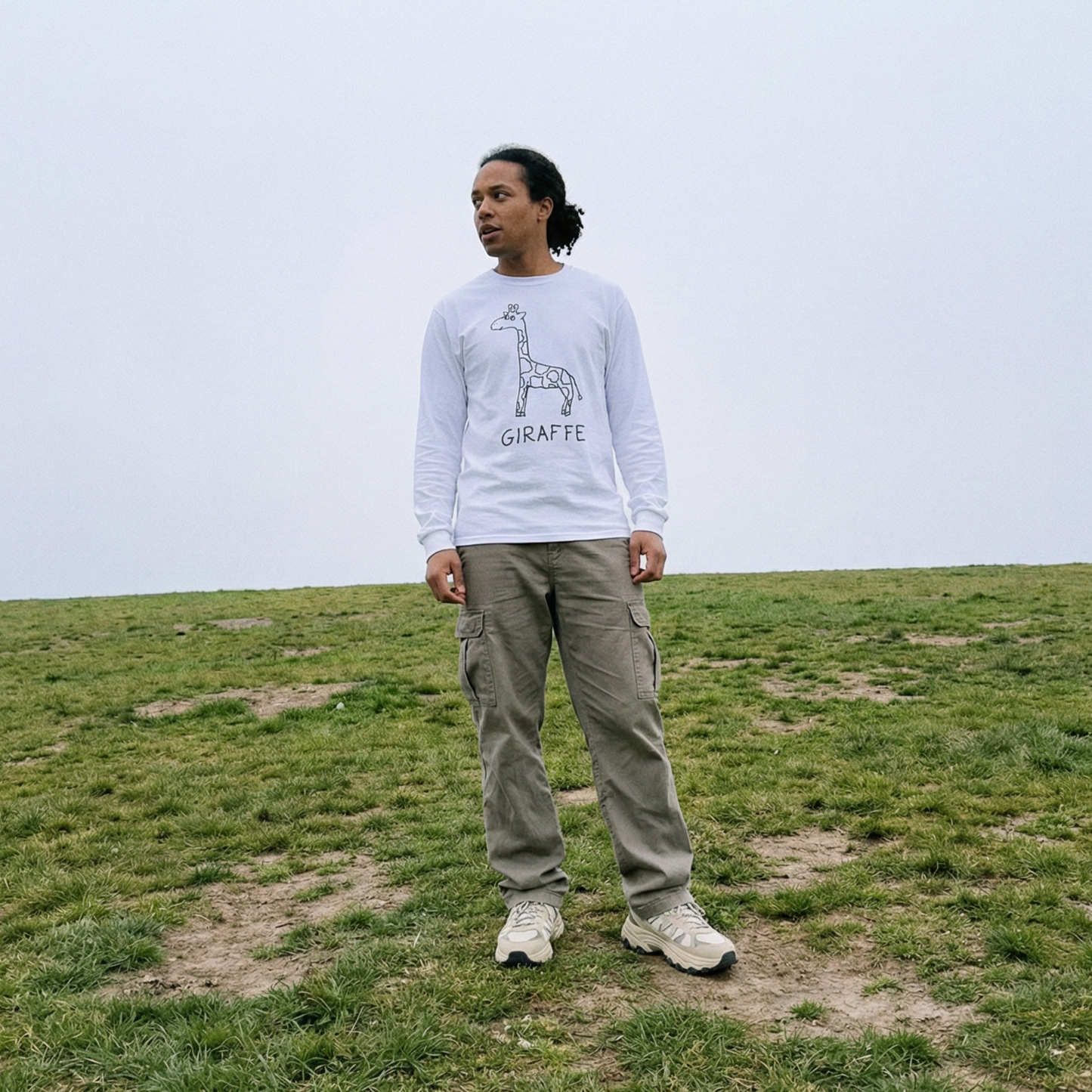 Person wearing a white sweatshirt with a  hand drawn giraffe graphic in a grassy field