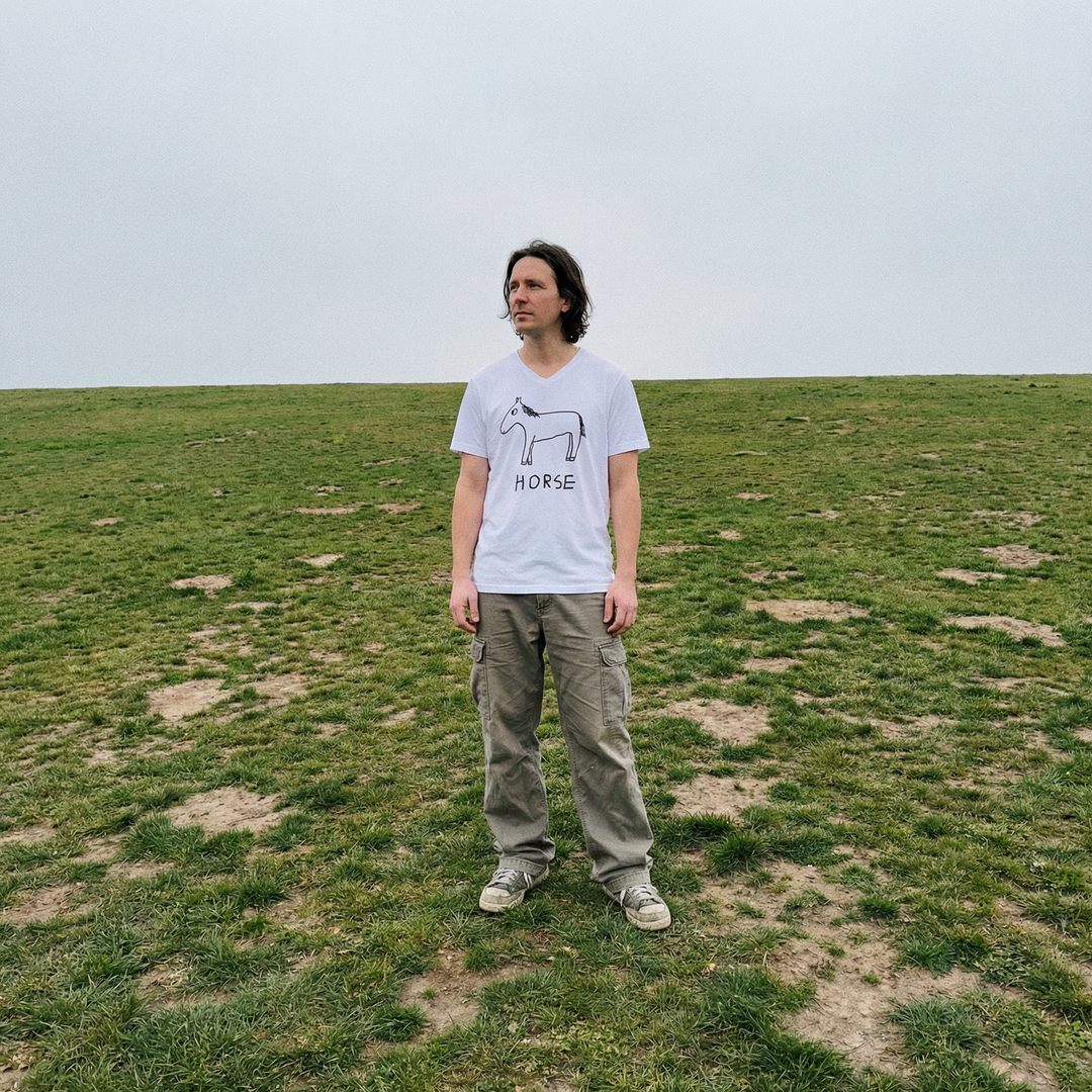 Model in horse v-neck tee in a wide rolling field, distant treeline behind them