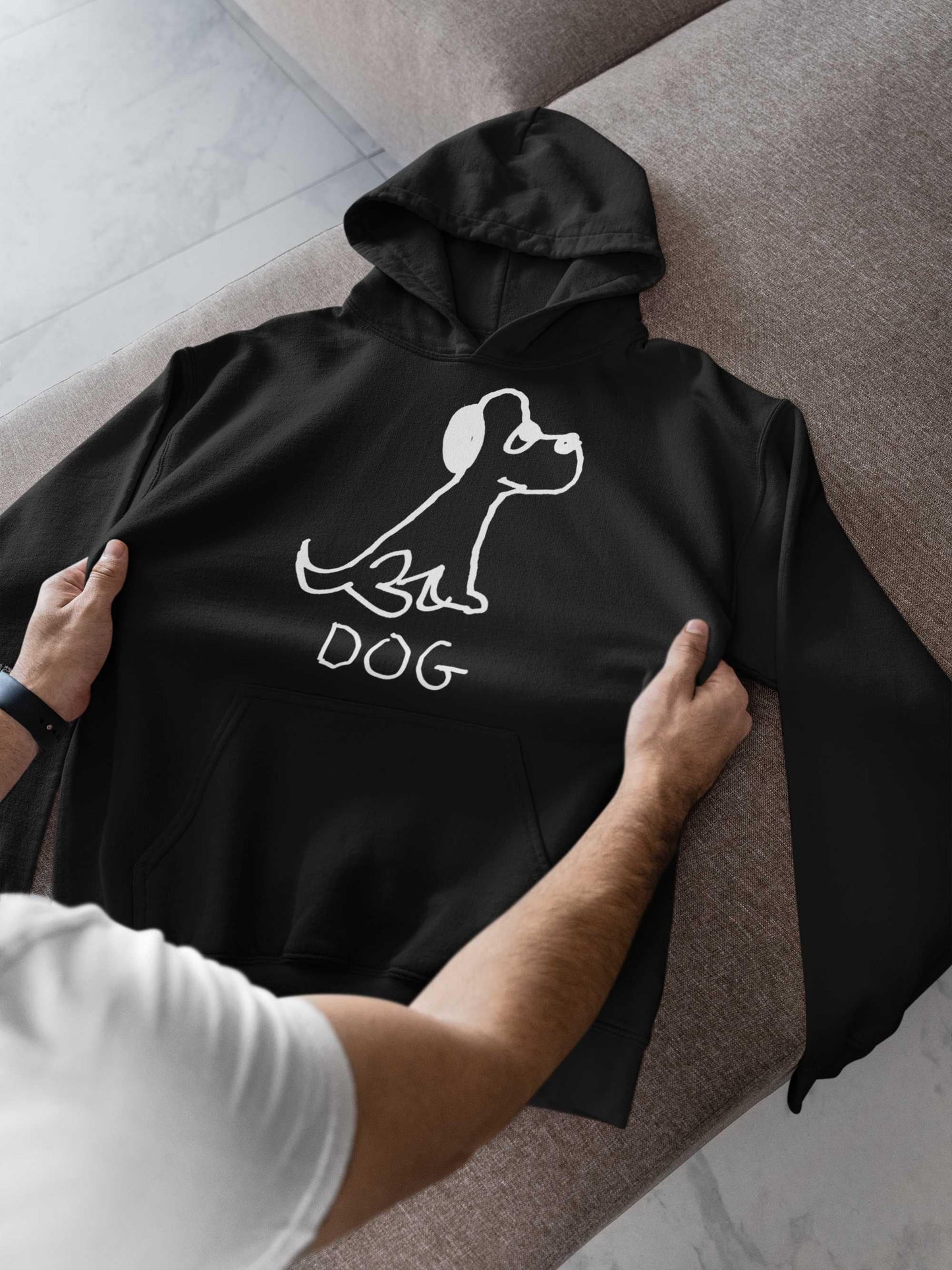 man checking out a black pullover hoodie sweatshirt featuring a crude marker black and white marker drawing of a cute dog with the word "DOG" handwritten underneath