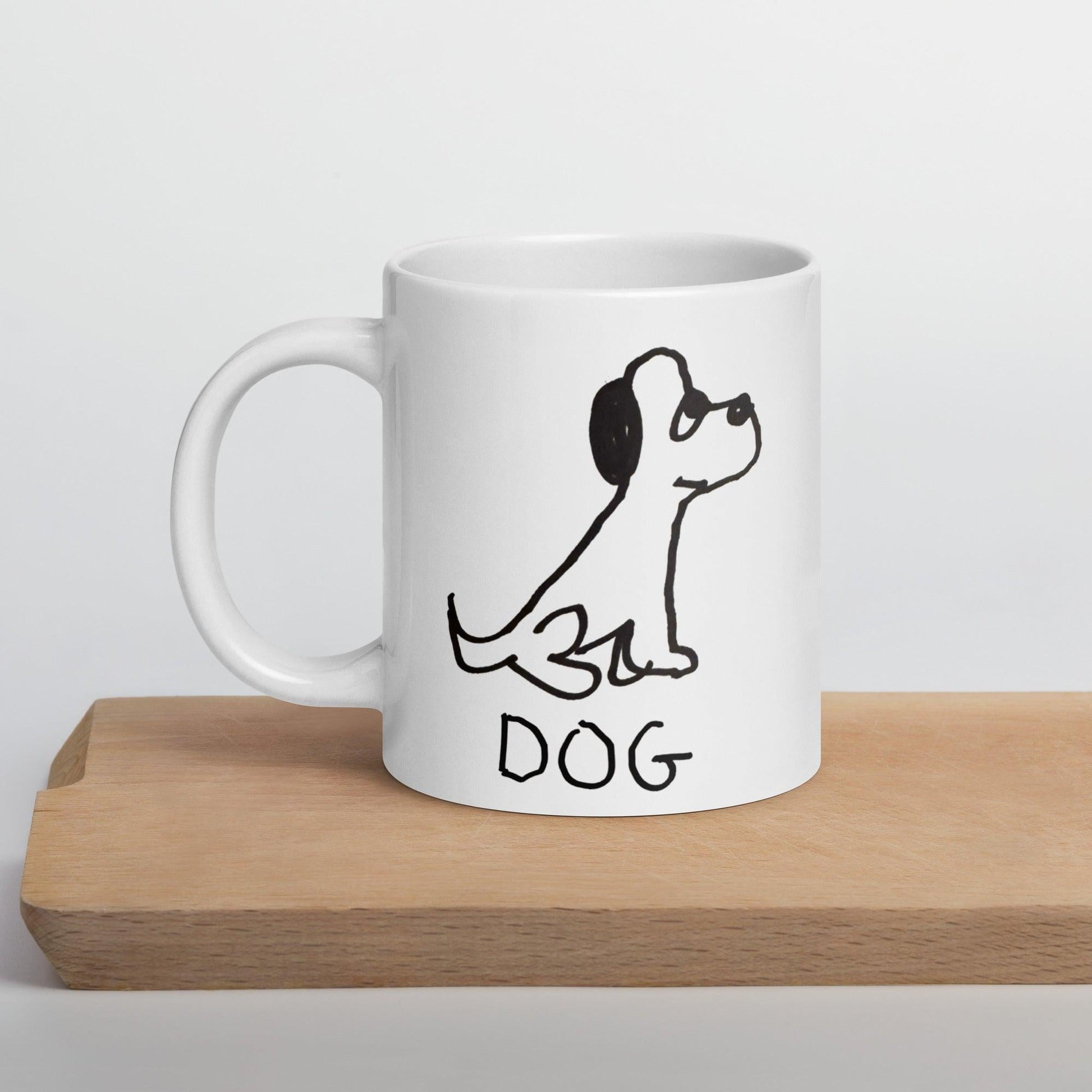 white coffee mug on wood surface  featuring a crude marker black and white marker drawing of a cute dog with the word "DOG" handwritten underneath
