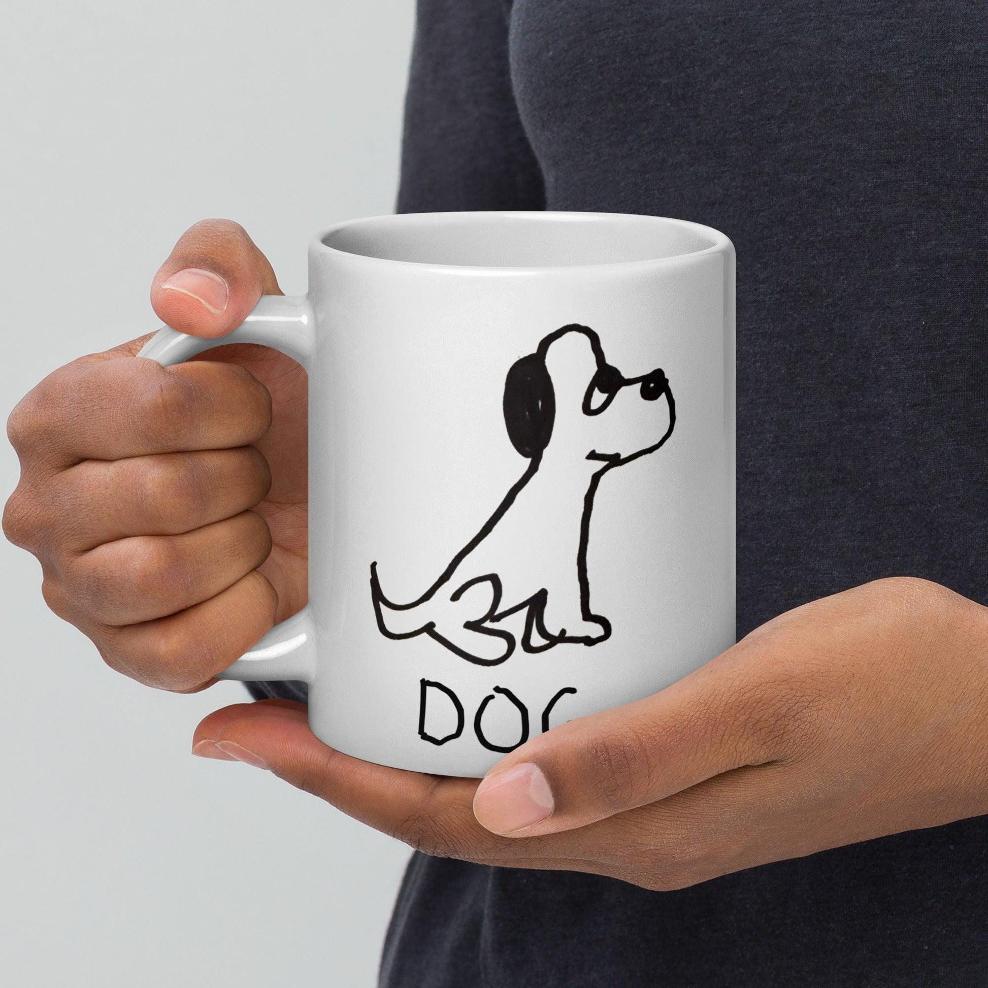 male hands holding a white coffee mug  featuring a crude marker black and white marker drawing of a cute dog with the word "DOG" handwritten underneath
