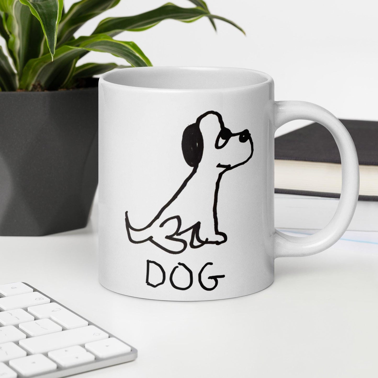 white coffee mug  featuring a crude marker black and white marker drawing of a cute dog with the word "DOG" handwritten underneath, sitting on office desk. 