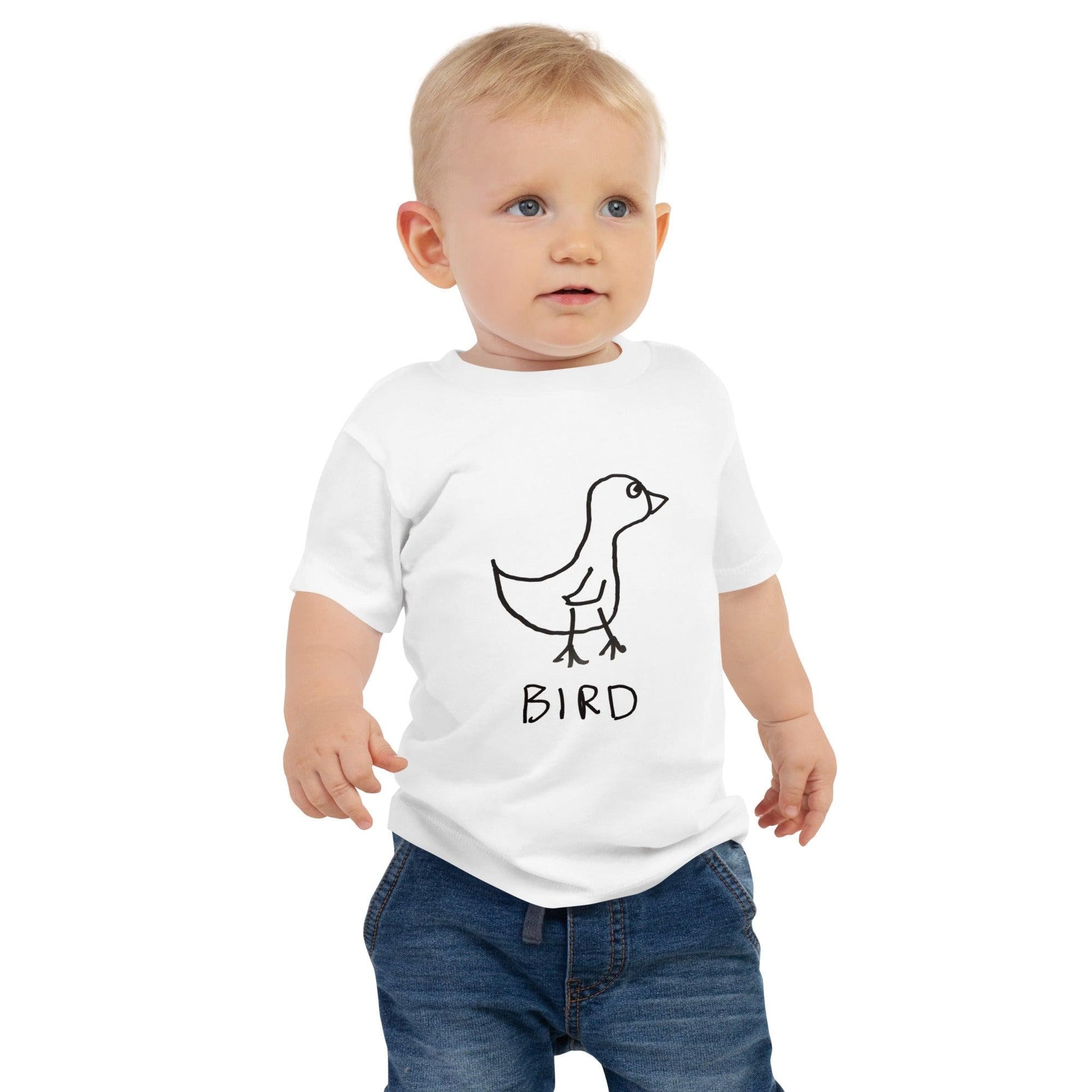 A cute toddler wearing a white tee shirt with a crudely drawn black marker drawing of a bird on it, with the word "Bird" underneath