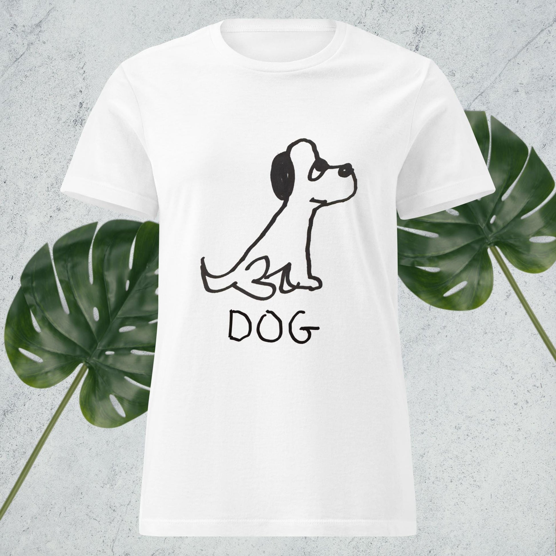 mockup of white women's fitted t-shirt featuring a crude marker drawing of a dog with the word "DOG" handwritten underneath, against a gray background with green leaves. 
