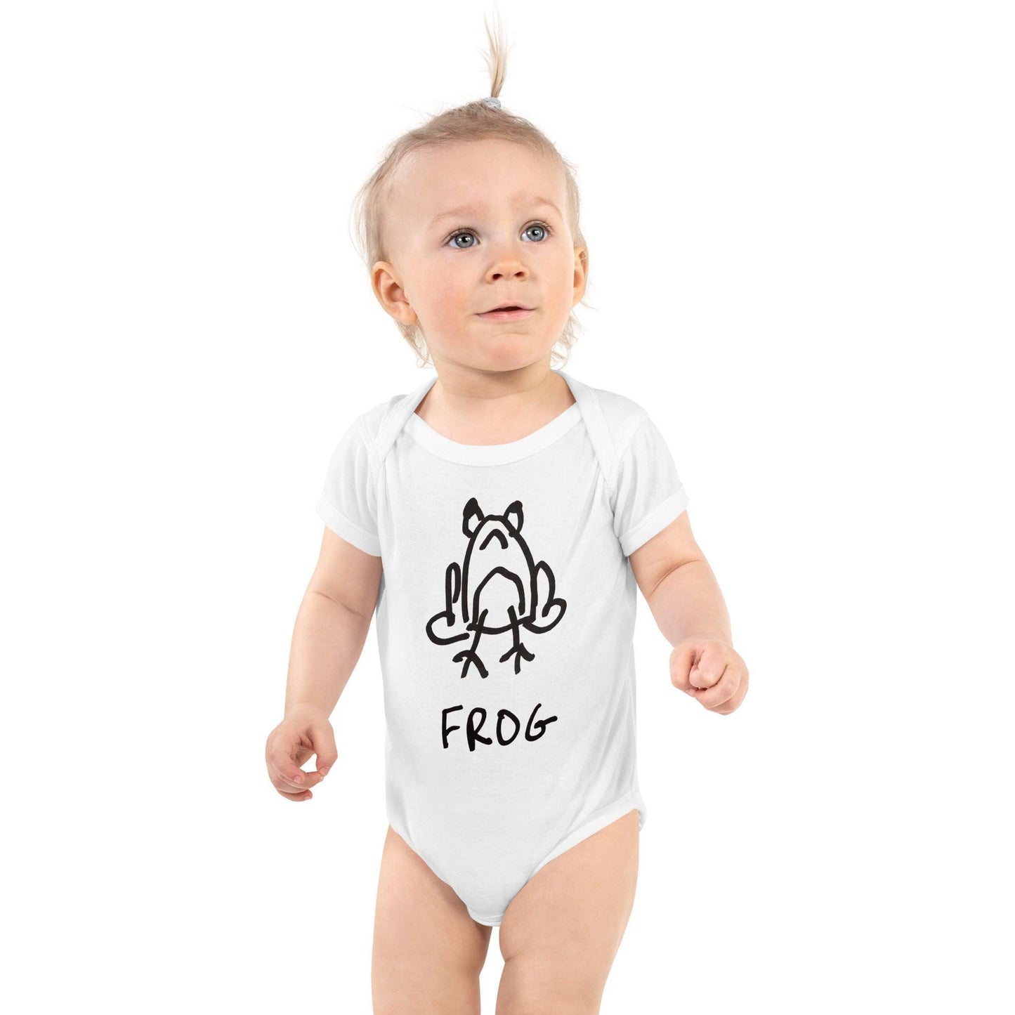 baby standing against white background wearing white baby onesie featuring a crude but cute black and white marker marker drawing of a cute frog with the word “FROG” handwritten underneath