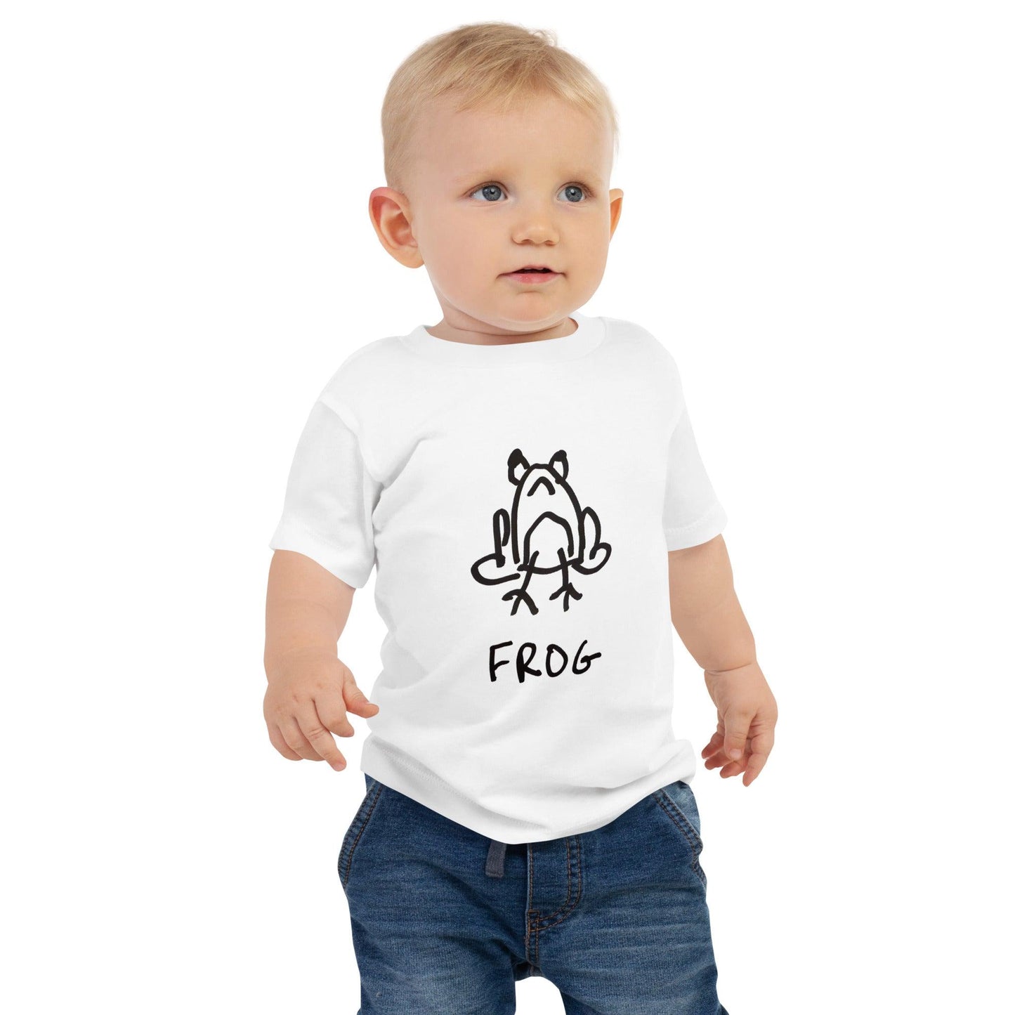 A toddler standing against a white background wearing a white toddler t-shirt featuring a crude but cute black and white marker marker drawing of a cute frog with the word “FROG” handwritten underneath