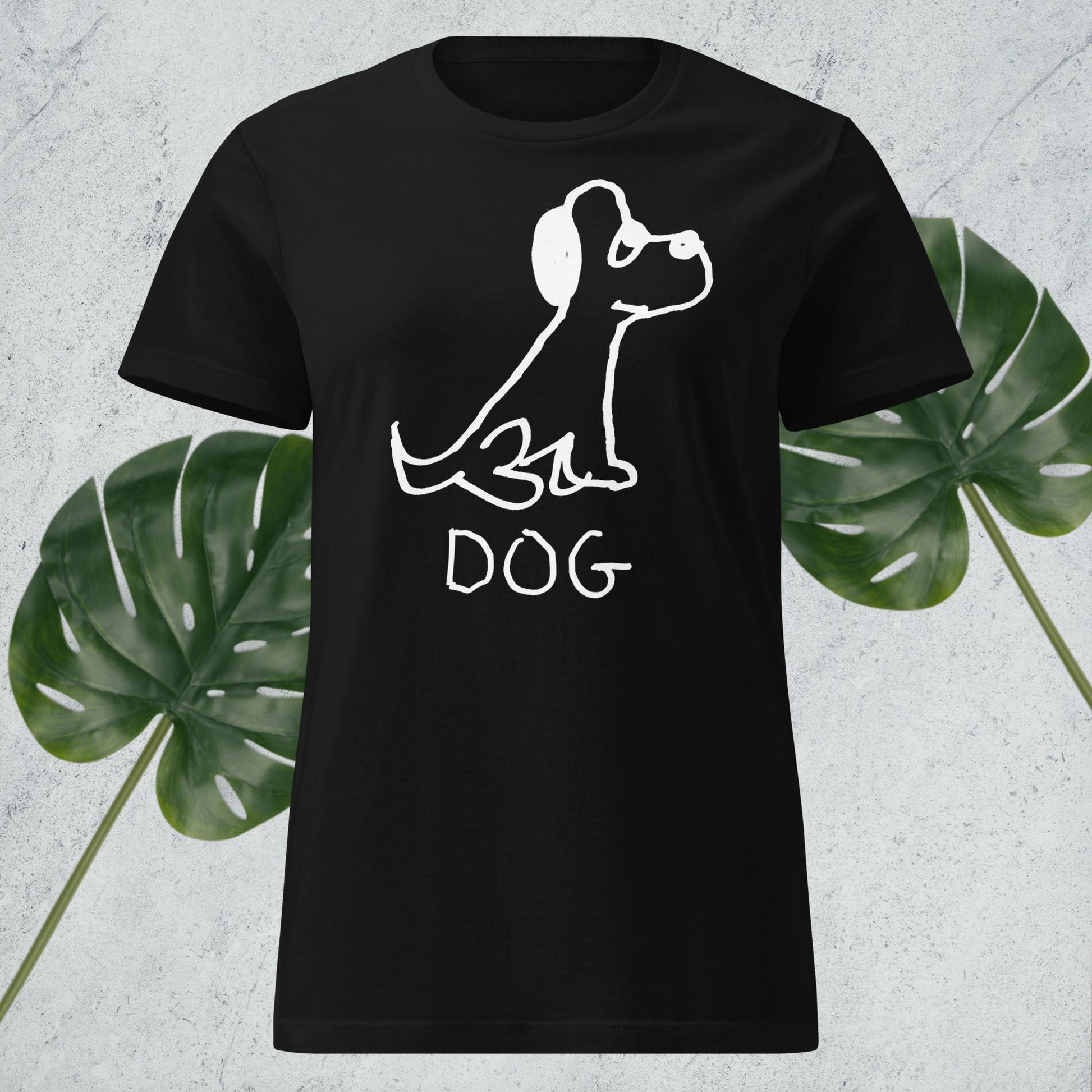 mockup of black women's fitted t-shirt featuring a crude marker drawing of a dog with the word "DOG" handwritten underneath, against a gray background with green leaves. 