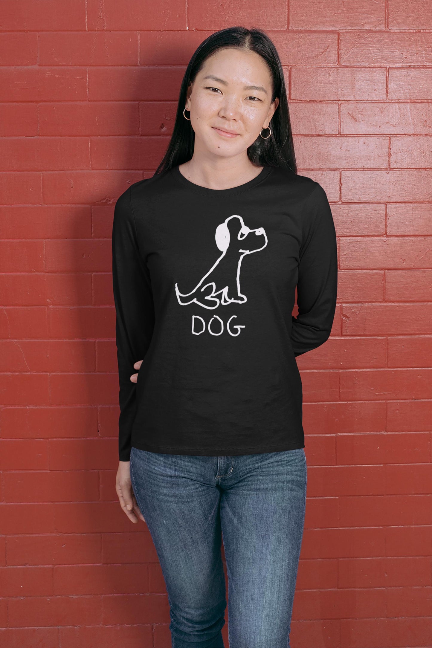 cool young woman wearing a black long-sleeve shirt White Long sleeve tee featuring a crude marker black and white marker drawing of a cute dog with the word "DOG" handwritten underneath on a polka dot background.  against a red brick wall.