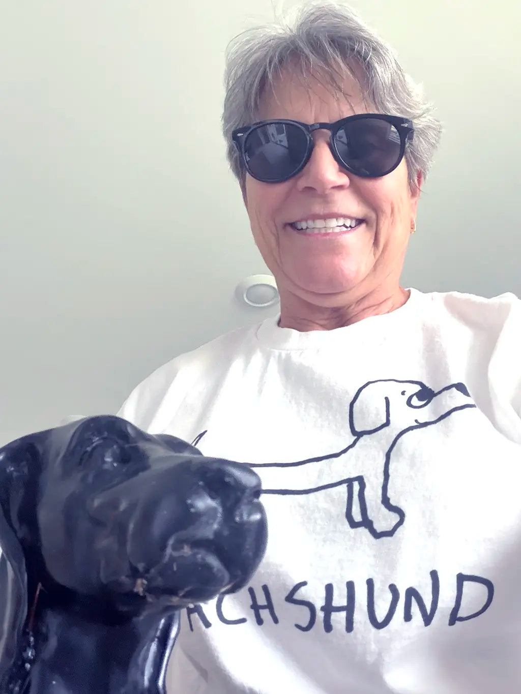 Woman with sunglasses, wearing a white t-shirt with a lo-fi hand-drawn dachshund graphic and text.