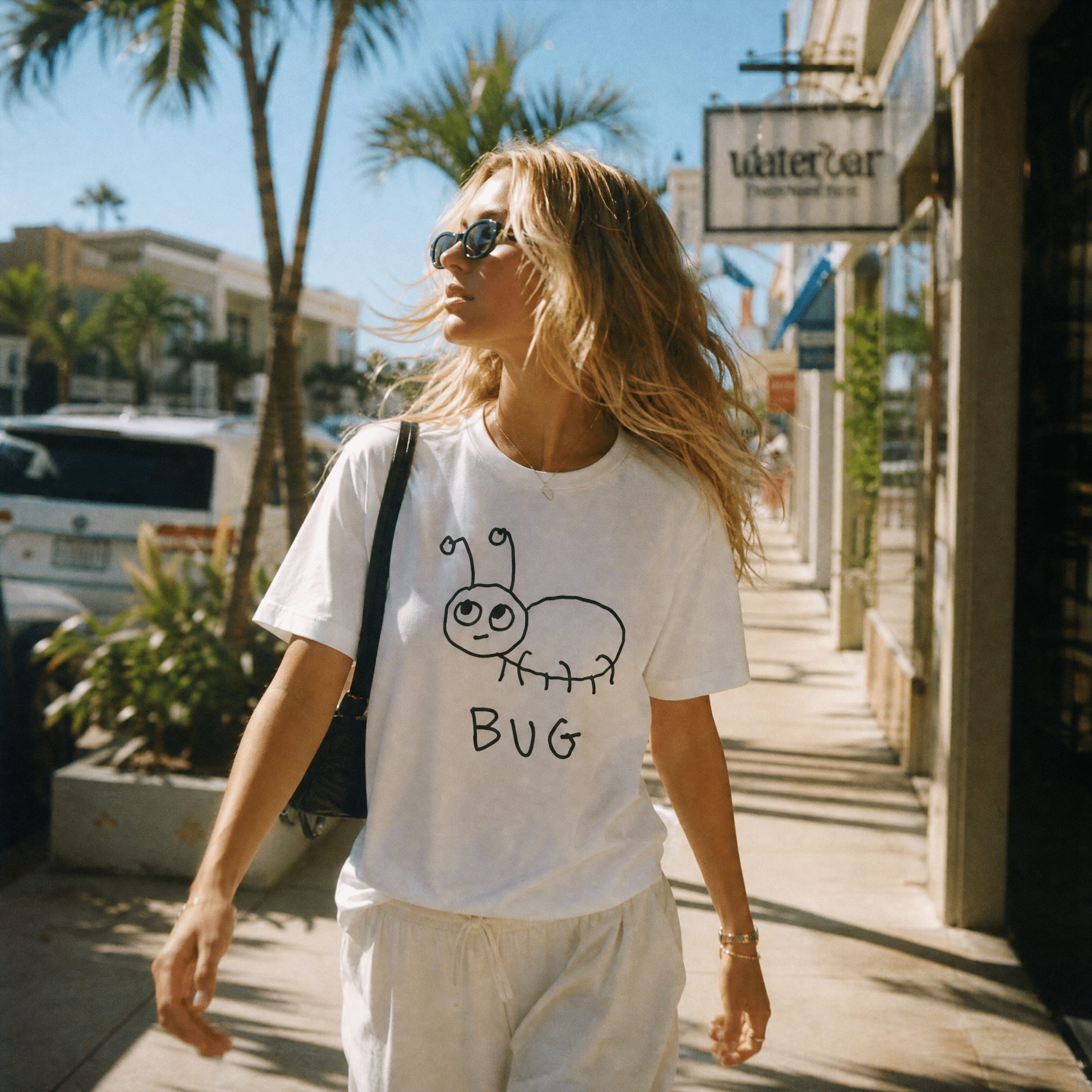 Woman walking a palm-lined beach town street in a lo-fi Bug Women's Relaxed T-Shirt in white