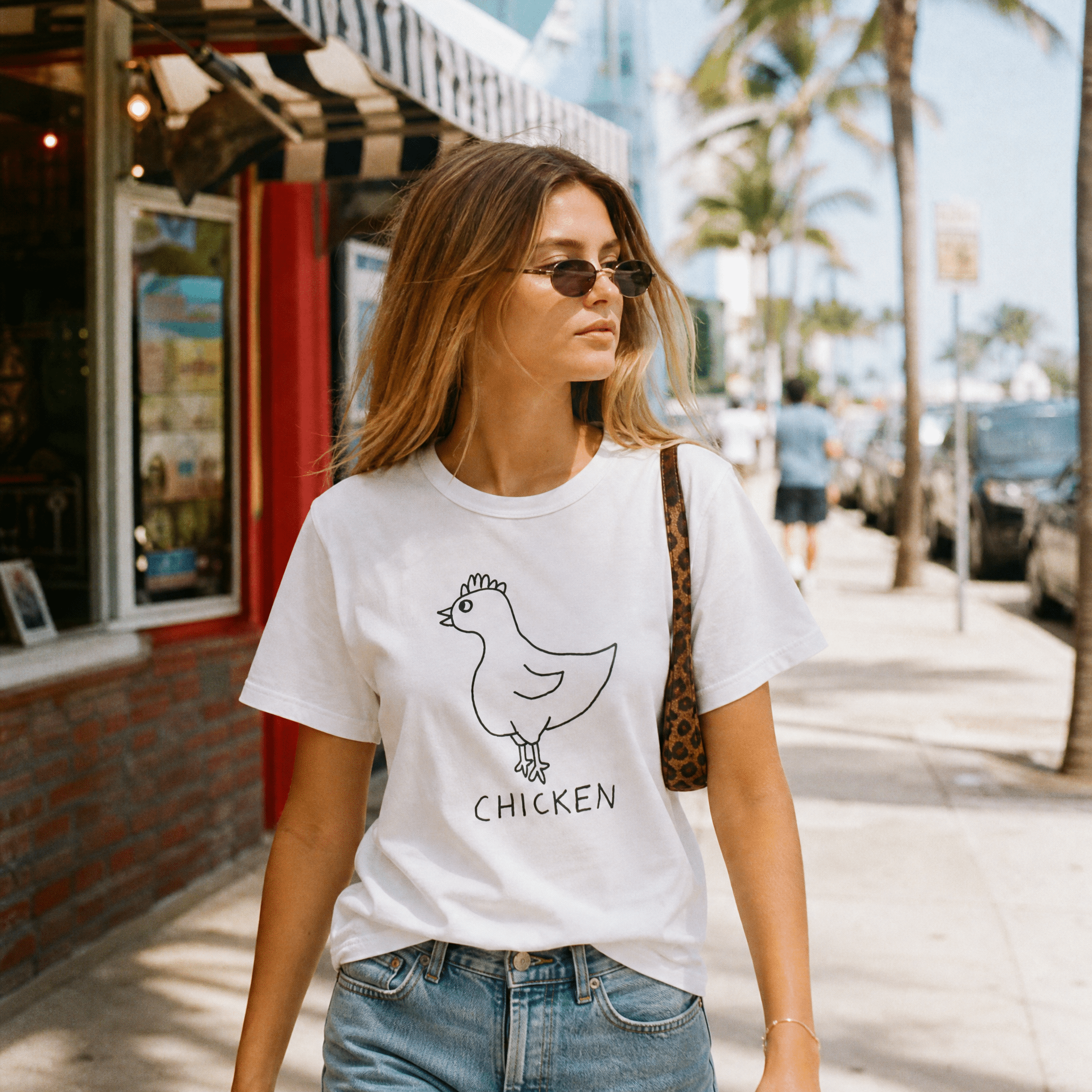 Woman walking a palm-lined beach town street in a lo-fi Chicken Women's Relaxed T-Shirt in white