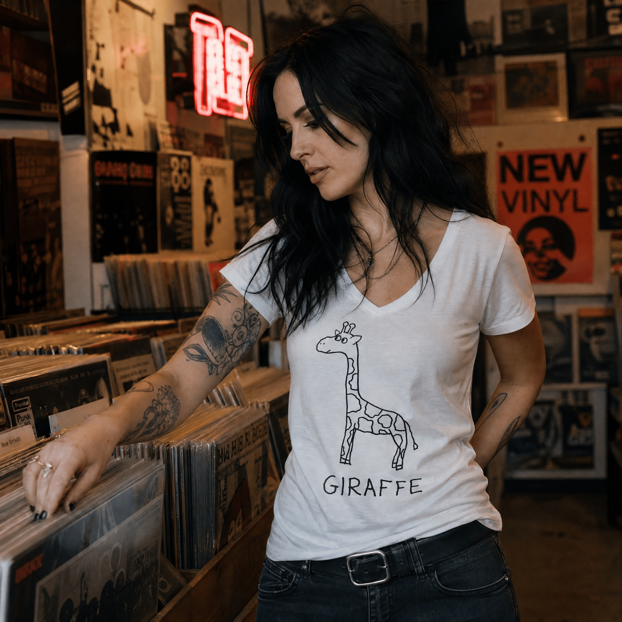 Dark-haired woman browsing records in a record store wearing a lo-fi Giraffe Women's V-Neck Tee