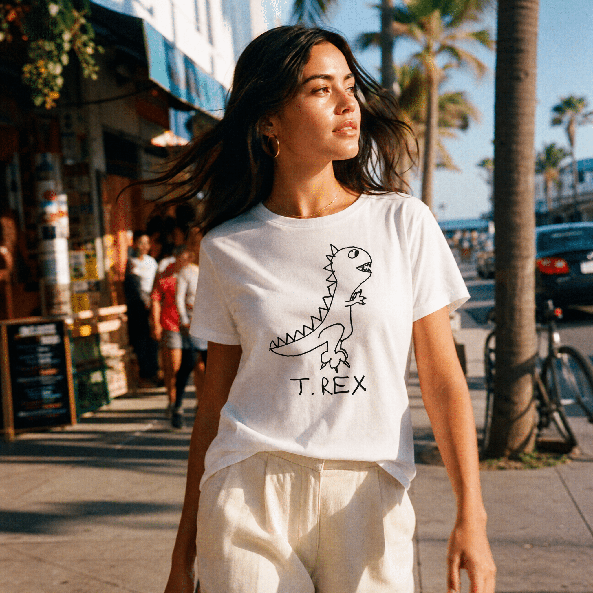 Woman walking a palm-lined beach town street in a lo-fi T. Rex Women's Relaxed T-Shirt in white