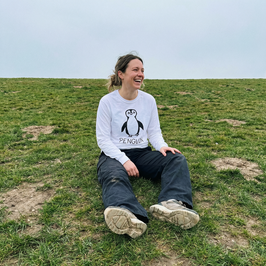 Model in a penguin long sleeve tee standing solo in a wide green field