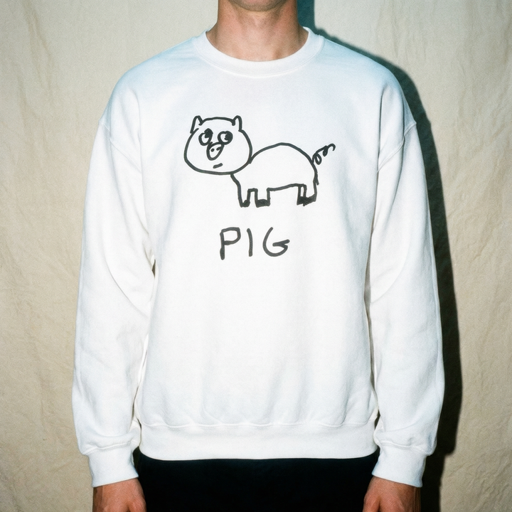 Model in a crewneck sweatshirt  with a lofi pig drawing graphic, against a beige background, soft warm lighting
