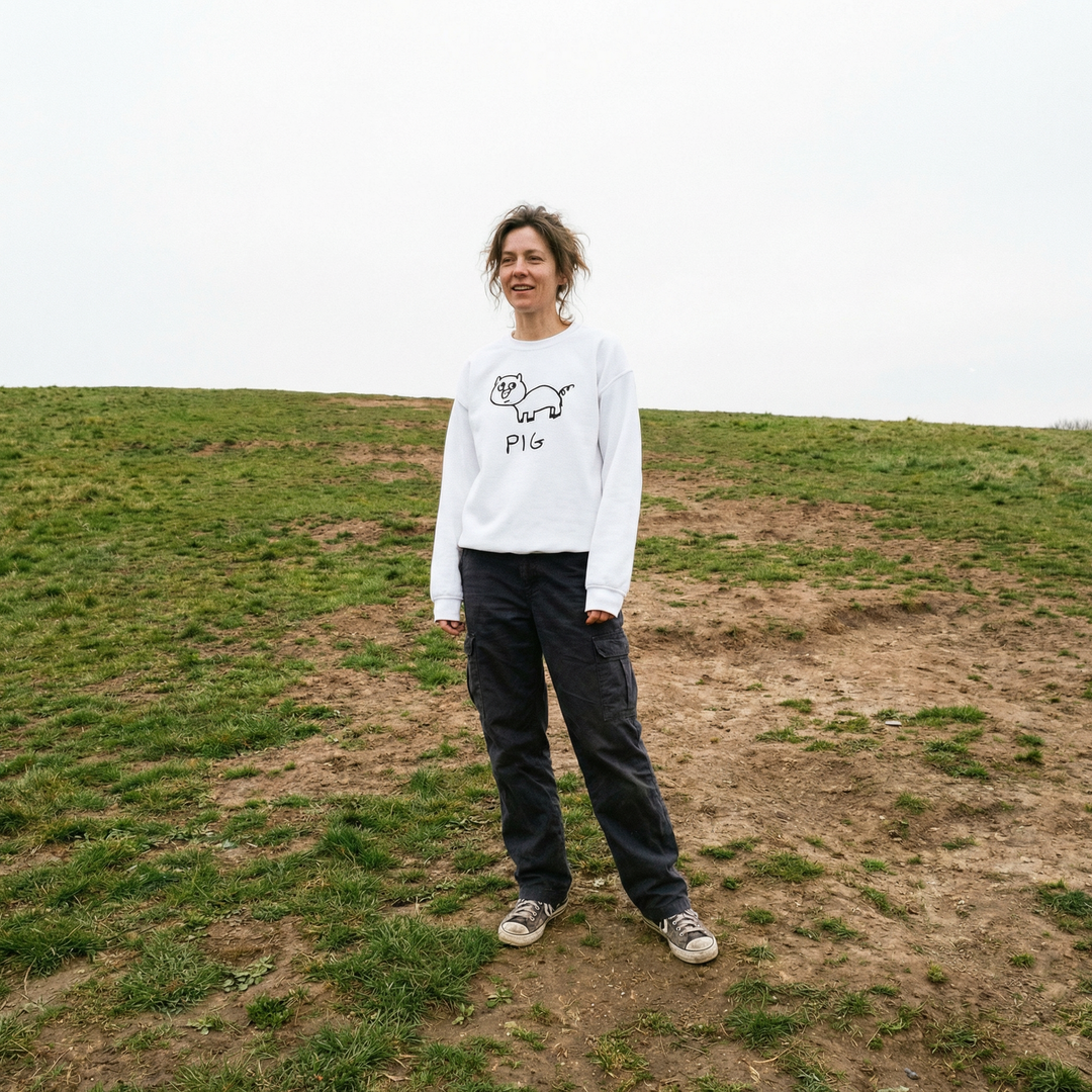 Model in a crewneck sweatshirt with a hand drawn pig graphic, standing in a grassy field, warm light, totally unbothered