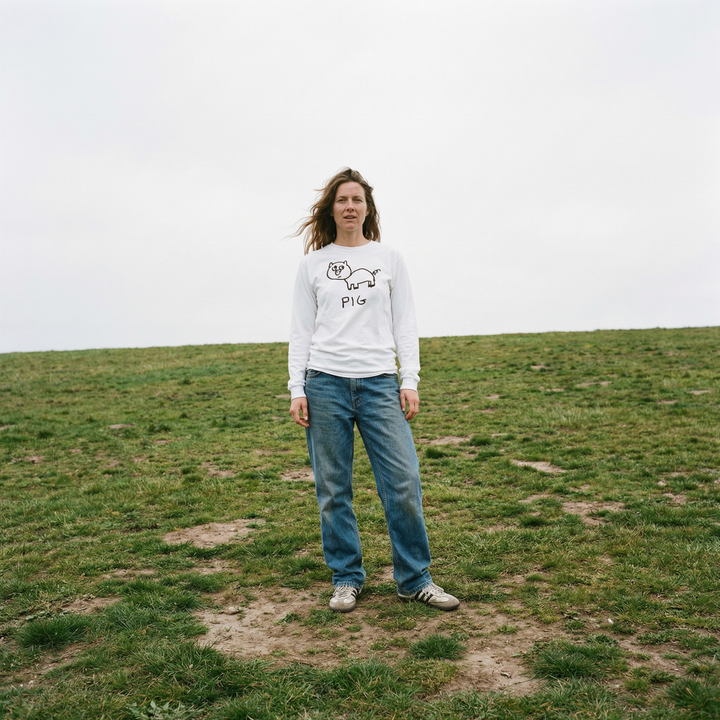 Model in a pig long sleeve tee standing at ease in a soft green grassy field
